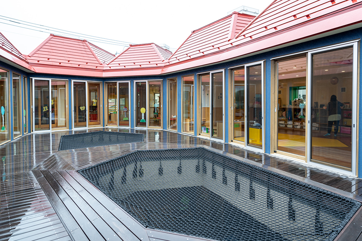 多面体が連なる園舎をつなぐ大きなネット遊具。中庭の砂場を見下ろせる。