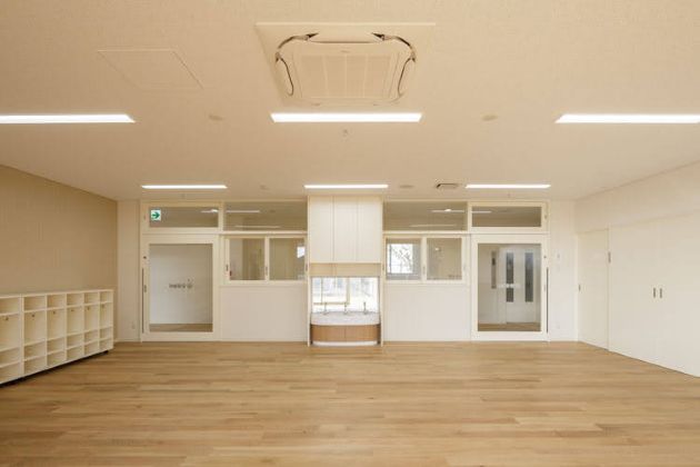 入口ドアも全面ガラスで開放的な幼児の保育室（写真は竣工時）。白い壁と木目の床があたたかい。